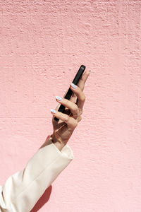 Elegant female hand holding mobile phone at pink background