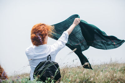 Rear view of woman holding scarf on grassy field against clear sky