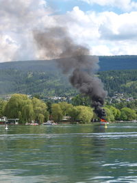 Distant view of burning boat in lake against sky