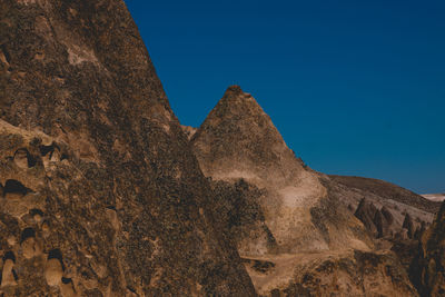 Low angle view of rocky mountain against clear blue sky