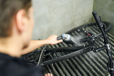 High angle of faceless male master washing modern bike with water in repair workshop