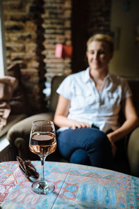 Close-up of wineglass on table with woman sitting on armchair in background