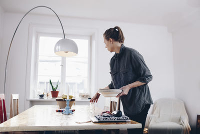 Side view of woman arranging plates on dining table at home