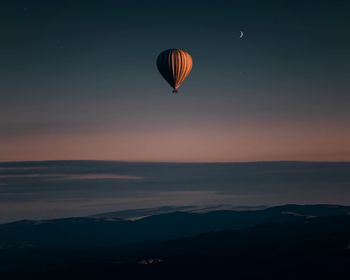 Hot air balloons flying over silhouette mountain against sky during sunset