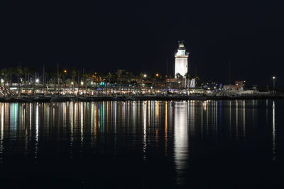 Illuminated buildings by river against sky at night