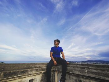 Portrait of young man sitting against blue sky