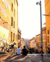 Rear view of people sitting on street amidst buildings in city