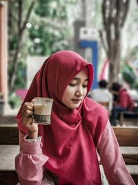 Young woman holding glass while sitting on seat