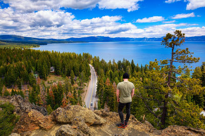 Rear view of woman standing on rock by lake against sky