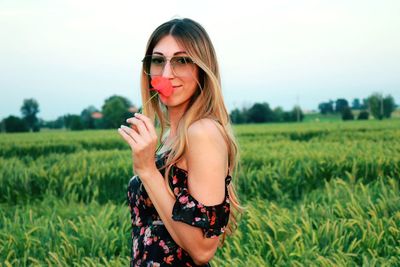 Portrait of young woman holding flower while standing on field