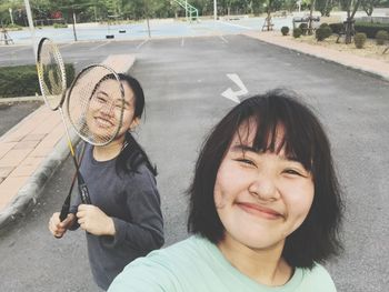 Close-up portrait of smiling women with badminton racket on road