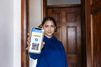 Young woman showing digital vaccine certificate on smart phone at home