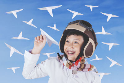 Close-up of boy playing with paper airplanes while standing against blue sky