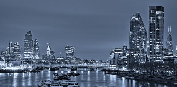 Bridge over river by buildings against sky in city