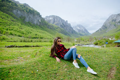 Young woman leaning on grassy field against mountains