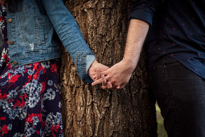 Midsection of people with holding hands against tree