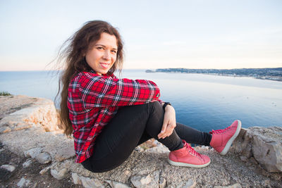 Young woman sitting on rock at shore