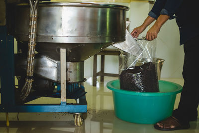 Low section of manual worker collecting roasted coffee beans from machinery in factory