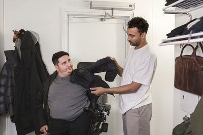 Career helping man in wheelchair putting jacket on