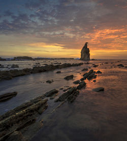 Rock formation on beach against sky during sunset