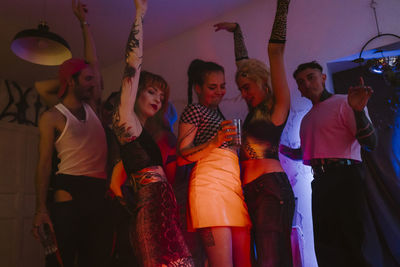 Carefree group of multiracial non-binary friends dancing with arms raised at nightclub