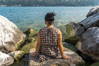 Rear view of woman looking at lake while sitting on rock