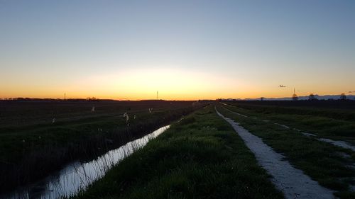 Road amidst field against clear sky during sunset