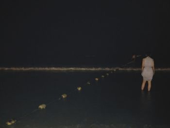 Rear view of woman standing by sea against sky at night