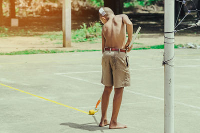 Rear view of shirtless man with umbrella standing on road