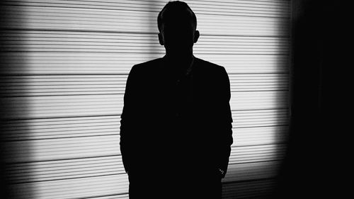 Silhouette businessman standing against blinds window