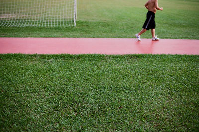 Low section of shirtless man jogging on track