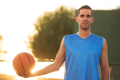 Portrait of man holding basketball against sky