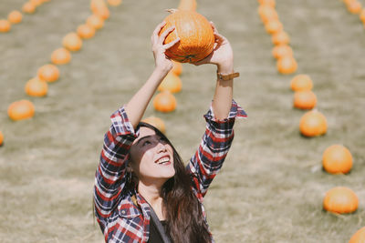Smiling young woman holding pumpkin at agricultural field