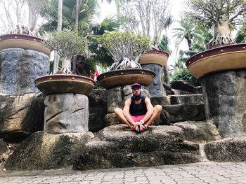 Woman sitting by fountain against plants