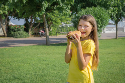 Happy teenage girl eating a burger in the park outdoors.
