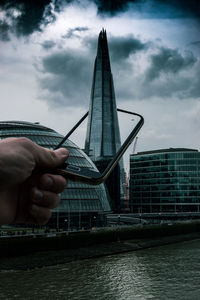 Digital composite image of cropped hand holding mobile phone amidst shard london bridge