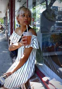 Young woman drinking glass while sitting by window