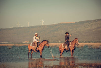 People riding horses at shore against sky