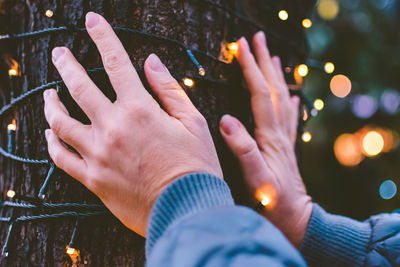 Cropped hands of person on illuminated lighting equipment on tree trunk at night
