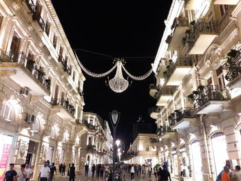 People walking on illuminated street amidst buildings in city