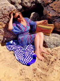 Full length of smiling woman sitting against rocks at beach