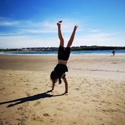 Full length of girl doing handstand on sand against sea at beach