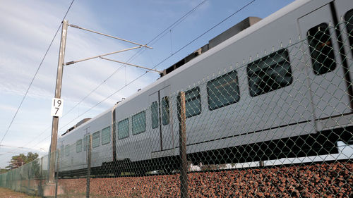 Low angle view of train by fence against sky