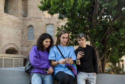 Friends using mobile phone while standing outdoors on the street.