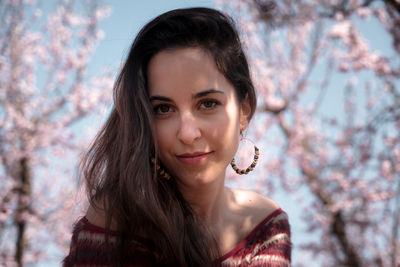 Portrait of smiling young woman against cherry blossoms and blue sky