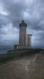 Lighthouse on sea against cloudy sky