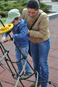 Mother assisting son in climbing on jungle gym at playground