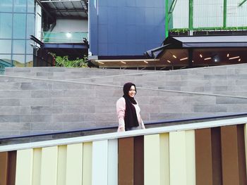 Portrait of woman standing against railing in city