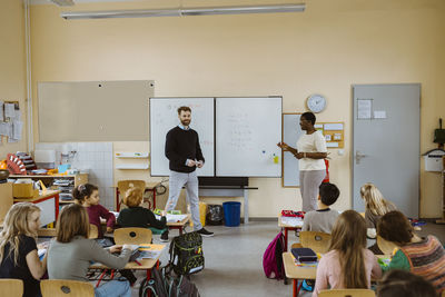 Male and female teachers teaching mathematics to pupils in classroom