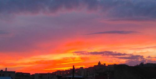 Silhouette buildings against dramatic sky during sunset